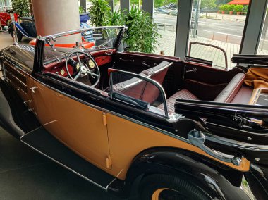 1930 model, krom aksanlı ve siyah çatılı, koyu kahverengiye boyanmış bir araba, yumuşak ışıklandırmanın altında kapalı alanda sergileniyor. Arabanın yan ve ön tarafı görülebilir, konforlu Redburgundy 'ye işaret ediyor.