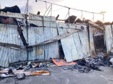 Hasarlı metal yapı muhtemelen yanmış, kısmen çökmüş bir çatı, erimiş yüzey parçalarıyla kararmış duvarlar ve yanmış eşyalar ile yanmış bir yangın sonrası dökülmüş.