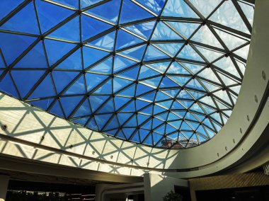 Geniş bir iç mekan, mavi-yeşil ışık ve gölge yansıtan kubbeli cam tavan. Tasarım zeminin yayını yansıtıyor, kıvrımlı bir yapı olduğunu gösteriyor. Tarafsız renkler ve sanayi.