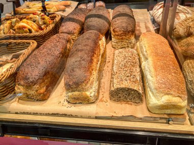 Altı çeşit taze pişmiş ekmek somunu ahşap bir tahtanın üzerinde yumuşak gölgeler ve değişik kabuk gölgeleriyle, kapalı bir pastane ortamında sergilenir.