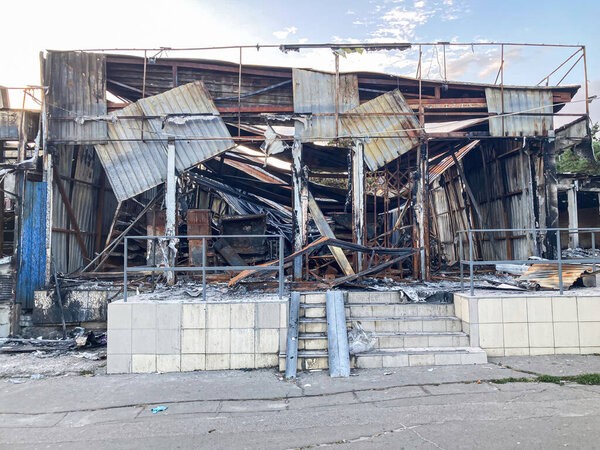Destroyed store, severe structural damage, charred interior, debris, twisted metal staircase, urban or industrial setting, natural lighting, no distinguishing marks, street level perspective, grays a
