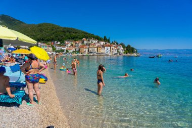 moscenicka draga, Hırvatistan - 08.28.2025: Güzel temiz su ve şehir manzaralı kalabalık plaj .