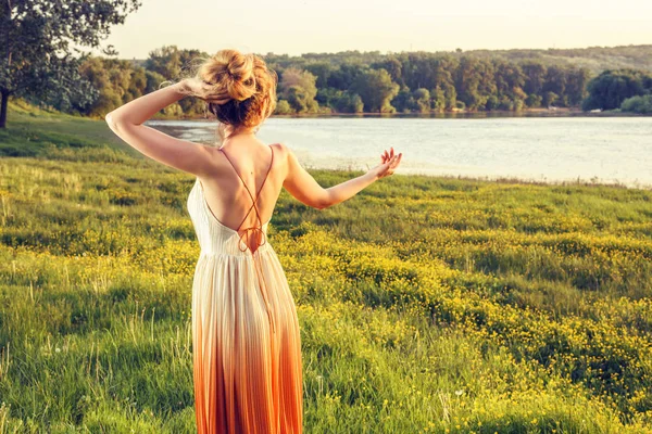 Mujer con un vestido largo y glamoroso al atardecer. Una chica encantadora. Hermosa vista del paisaje, disparado desde la espalda —  Fotos de Stock