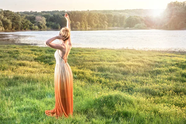 Woman watching the sunset in a long glamorous dress. Lovely girl. Beautiful landscapes view, shot from the back