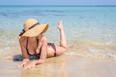 Kıbrıs'ta sahilde döşeme kadın. Şapka ve swimsuite. Güzel yaz deniz manzaralı. Güneşli gün tadını