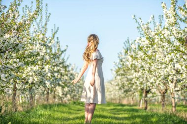 Baharda çiçek açan bir bahçede bir kadın. Güneşli sıcak günün tadını çıkarıyorum. Retro tarzı elbise. Renkli bahar havaları