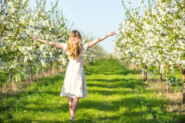 Woman in a blooming orchard at springtime. Enjoying sunny warm day. Retro style dress. Colorful spring moods