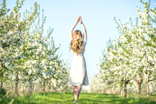 Mujer en un huerto floreciente en primavera. Disfrutar de un día soleado y caluroso. Ropa de estilo retro. Humores de primavera llenos de color —  Fotos de Stock