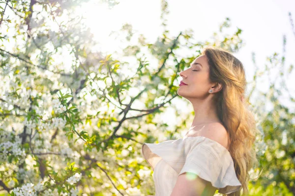 Mujer en un huerto floreciente en primavera. Disfrutar de un día soleado y caluroso. Ropa de estilo retro. Humores de primavera llenos de color —  Fotos de Stock