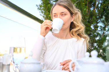Üzgün kadın bir fincan kahve içiyor. Beyaz elbiseli sarışın kız. Açık hava portreleri