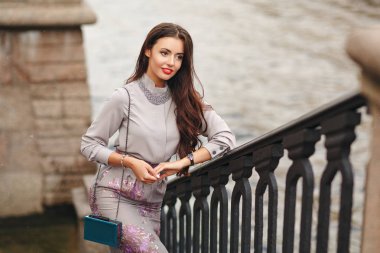 Güzel, göz alıcı ve şık bir esmer kız gülümser ve şehir içinde bir köprü üzerinde duruyor. Street Style