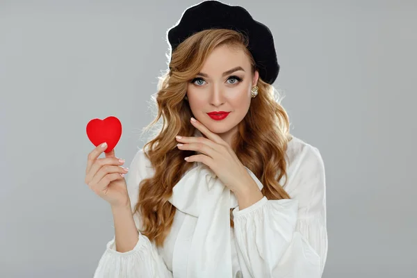 Una chica muy hermosa con labios rojos sostiene un corazón rojo en su han — Foto de Stock