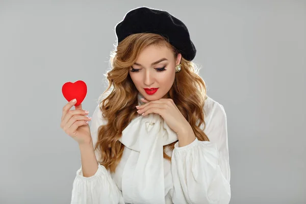 Uma menina muito bonita com lábios vermelhos segura um coração vermelho em seu han — Fotografia de Stock
