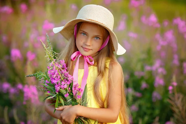 Una niña con un vestido amarillo y sombrero, sosteniendo flores lila i —  Fotos de Stock