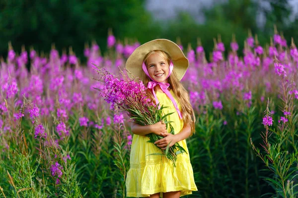 Una niña con un vestido amarillo y sombrero, sosteniendo flores lila i —  Fotos de Stock