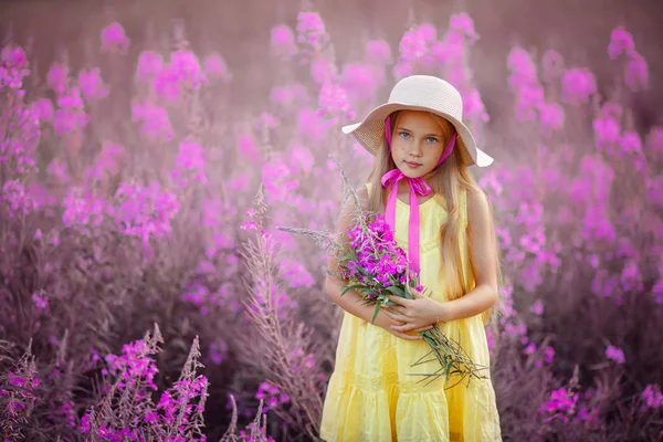 Een klein meisje in een gele jurk en muts, holding lila bloemen ik — Stockfoto