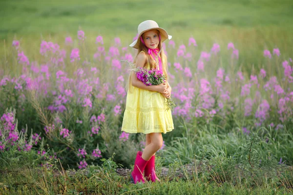 Uma menina em um vestido amarelo e chapéu, segurando flores lilás i — Fotografia de Stock