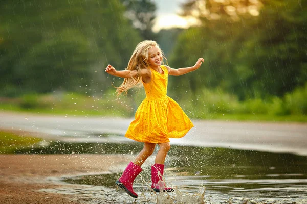 Een klein meisje in een gele jurk glimlacht en loopt door de pudd — Stockfoto