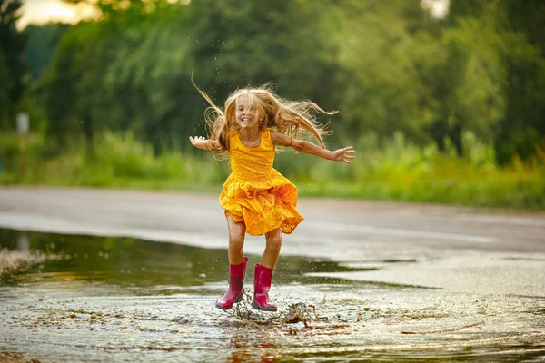 Een klein meisje in een gele jurk glimlacht en loopt door de pudd — Stockfoto