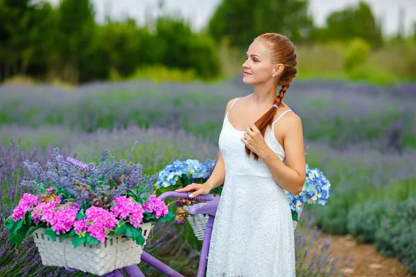 Chica pelirroja con una coleta en un vestido blanco en una bicicleta púrpura —  Fotos de Stock