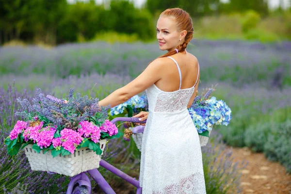 Menina de cabelos vermelhos com um pigtail em um vestido branco em uma bicicleta roxa — Fotografia de Stock