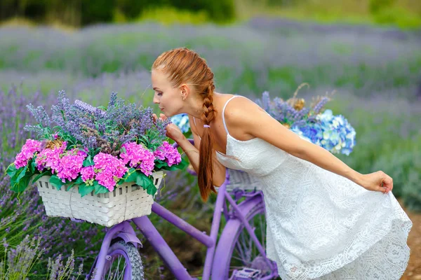 Chica pelirroja con una coleta en un vestido blanco en una bicicleta púrpura —  Fotos de Stock