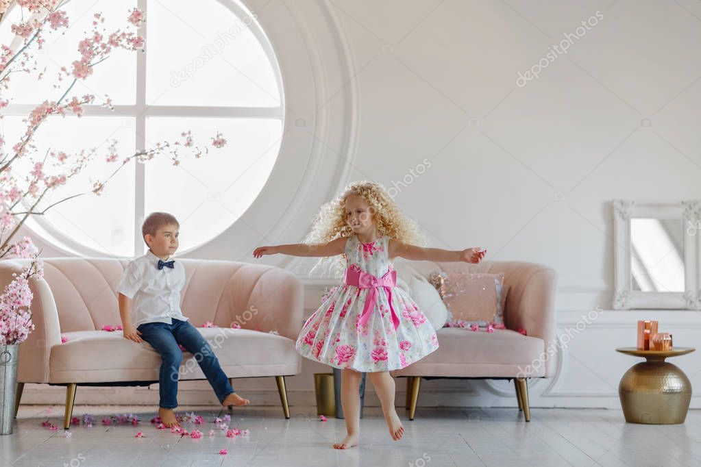 Cute girl blonde in a pink dress is dancing, a charming boy is l