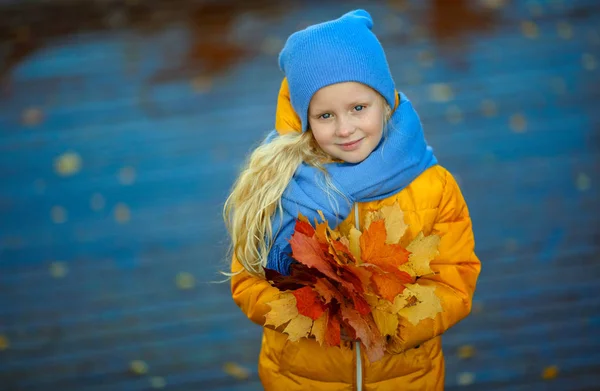 Beautiful little blonde girl with blue eyes in a yellow jacket s — Stock Photo, Image