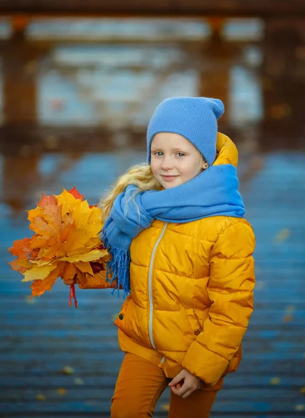 Vacker liten blond flicka med blå ögon i en gul jacka — Stockfoto