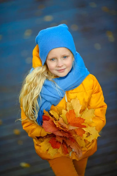 Mooi klein blond meisje met blauwe ogen in een geel jasje — Stockfoto