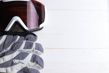 Kışlık eldivenler ve gözlükler beyaz, doğal tahta masa arka planında. Kayak ya da snowboard kavramı. Sağ taraftaki boşluğu kopyala. Düz üst görünüm.