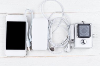 Beyaz teknoloji, doğal ahşap masa arka planında. Elektrik bankası, kablo, kulaklık, kamera, akıllı telefon. Düz üst görünüm.
