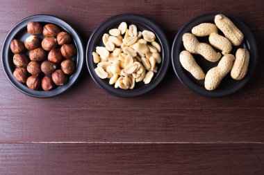 Koyu bir tabakta fındık ve fıstık. Kahverengi doğal masa. Düz manzaralı. Alta uzayı kopyala. Vejetaryen gıda konsepti.