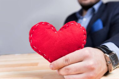 Sevgililer Günü 'nde kırmızı kalp tutan zarif genç bir adam. Mavi takım. Süslü saat. Doğal ahşap masa..