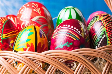 Renkli paskalya yumurtalarıyla hasır sepete yakın çekim. Ilık güneş ışığı parlıyor.