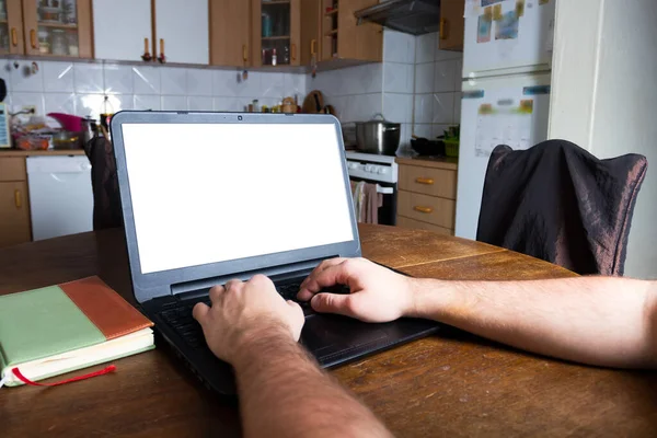 Man typing on a laptop computer in vintage kitchen. Blank white screen ready for mockup. Notepad. Old retro scratched wooden table.