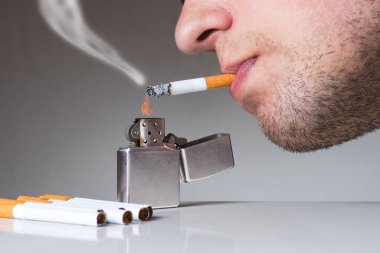 Genç adam klasik çizilmiş çakmakla sigara içiyor. Nikotin ve tütün bağımlılığı soyut bir kavram.