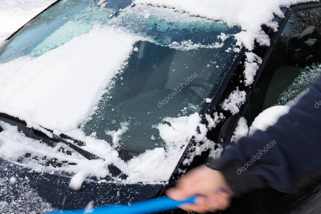 Man removing snow with a brush from his black car. Motion blur.