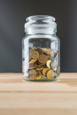 Doğal ahşap arka planda altın sikkeleri olan kavanoz. Para tasarrufu soyut kavramı.