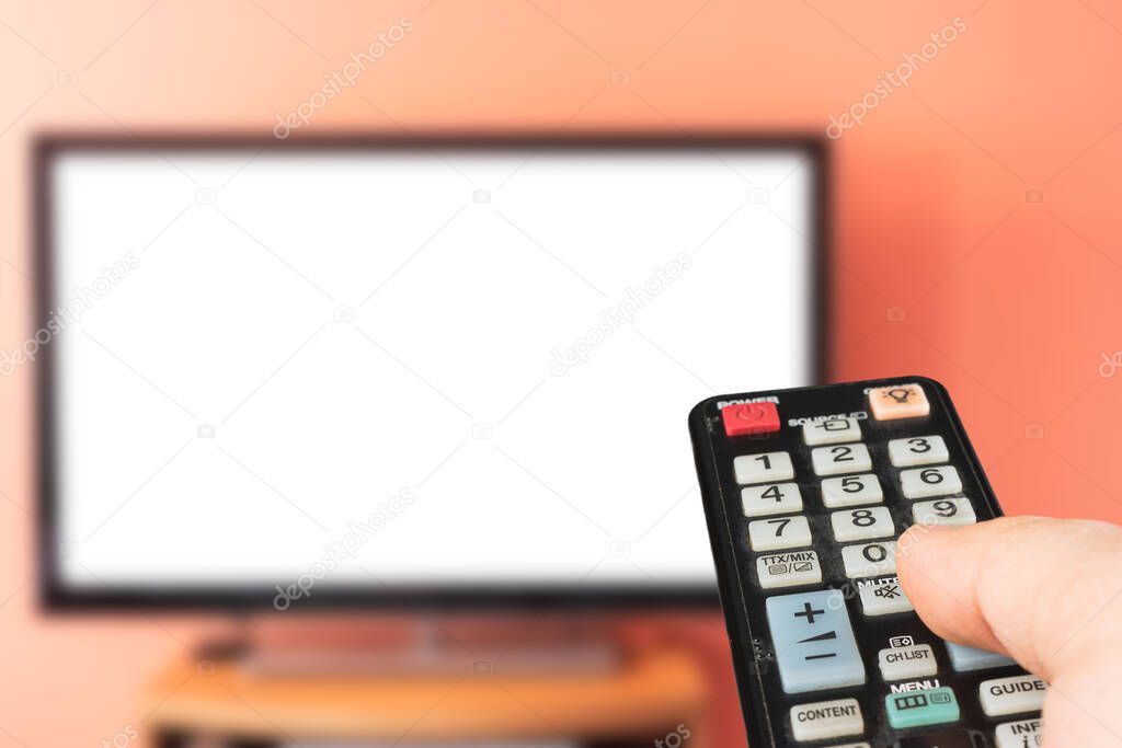 Caucasian man watching TV at home with white screen. Changing channels and adjusting volume with television remote control. 