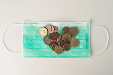 Avrupa sikkeleri yeşil koruyucu maskenin üzerinde duruyor. Tıbbi tedavi veya salgın maliyetleri ve soyut harcamalar.