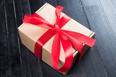 Kırmızı kurdeleli doğal kağıt kutu siyah doğal ahşap masa. Noel ya da Sevgililer Günü soyut kavramı.