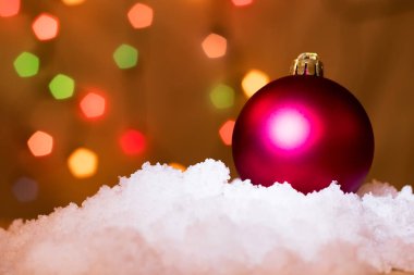 Karda noel ağacı süsü. Renkli ağaç ışıkları arka planda. Uzayı sola kopyala.