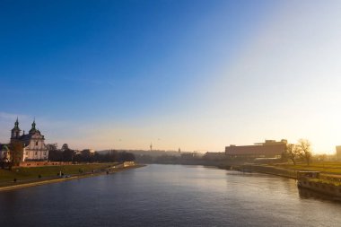 Gün batımında Krakow şehrinin ikonik manzarası. Sıcak öğleden sonra ışığı. Mavi gökyüzü. Geniş nehir.