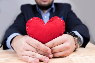 Sevgililer Günü 'nde kırmızı kalp tutan zarif genç bir adam. Mavi takım. Süslü saat. Doğal ahşap masa..