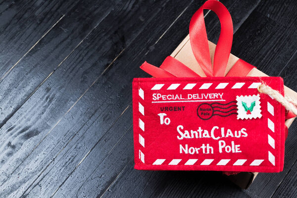 Красное письмо к Санта-Клаусу с бумажной коробкой с ленточным бантом на черном натуральном деревянном столе. Рождественский подарок или представить ребенка фантазии концепции. Пространство для копирования слева
.
