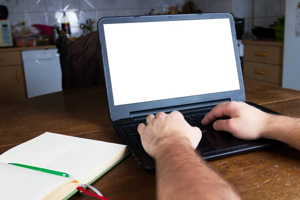 Man typing on a laptop computer in vintage kitchen. Blank white screen ready for mockup. Notepad. Old retro scratched wooden table.