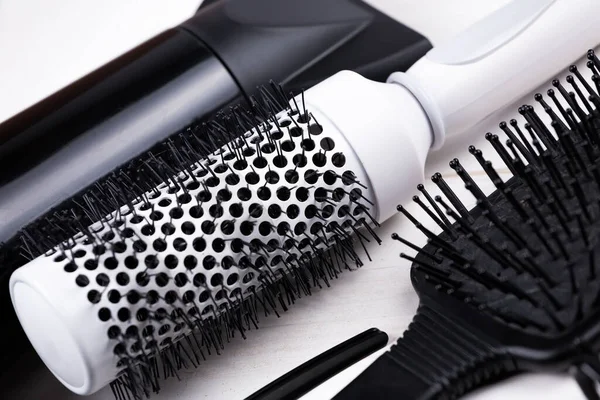 Black and white hair styling tools. Brush, dryer, clip on white natural wooden table background.