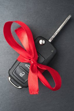 Siyah arka planda kırmızı fiyonklu araba anahtarı. Noel ya da Sevgililer Günü hediyesi ya da şu anki soyut kavram. Dikey oryantasyon. Düz üst görünüm.