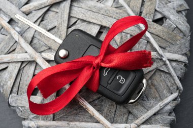 Siyah levha arka planında, tahta bir kalbe kırmızı fiyonk takılmış araba anahtarı. Noel ya da Sevgililer Günü hediyesi ya da şu anki soyut kavram.